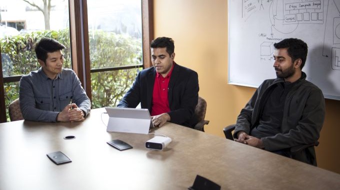 Three people at a conference table using a tablet.