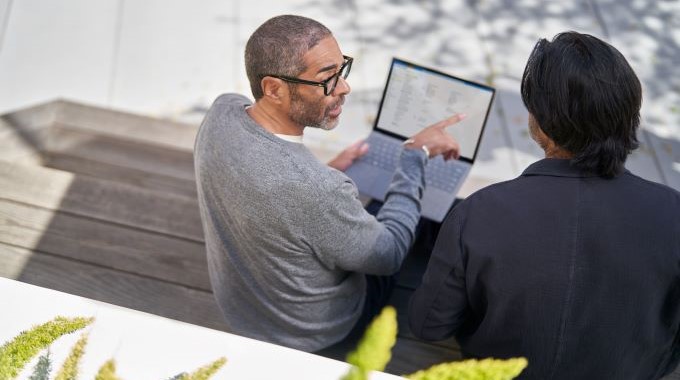 2 people talking on a bench with a laptop on their lap