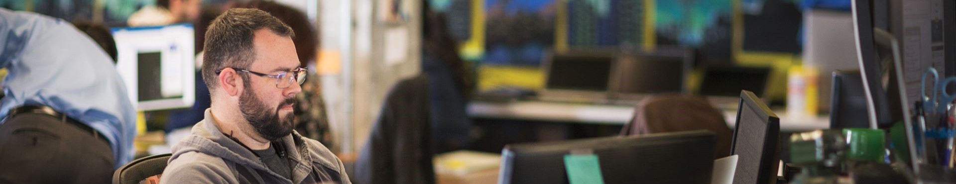 Man wearing glasses working at his desk on a desktop computer