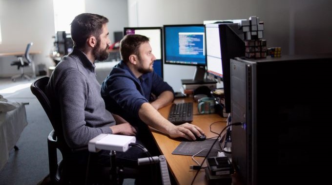 Men working on multiple monitor setup together