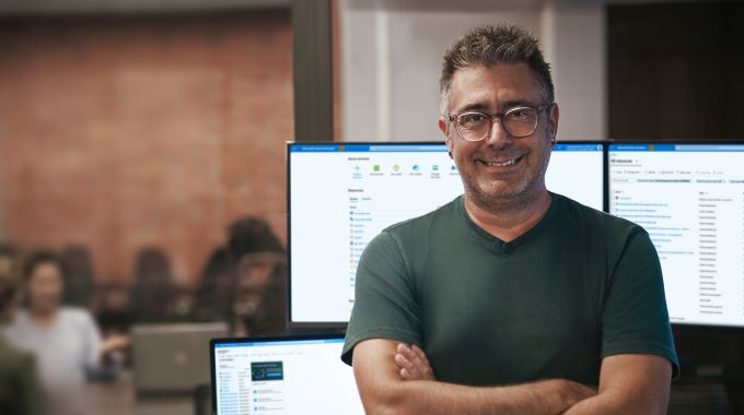 Developer portrait in context. Developer and IT integrator is camera facing. Background is FinTech. Investment and customer meeting along with developer. Monitors showing real-time data, analytics and insights powered by Azure.