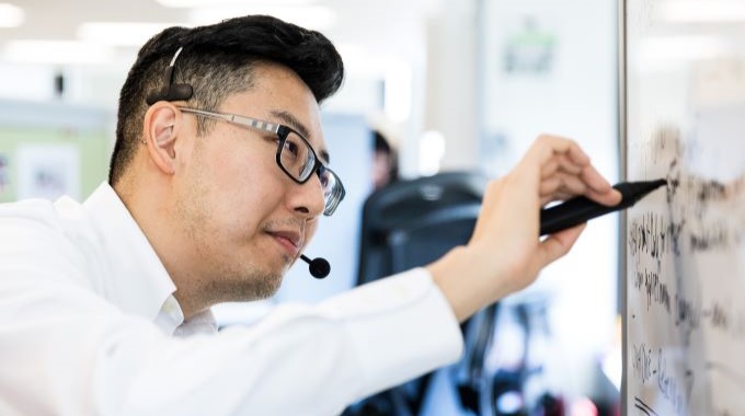 Man writing on whiteboard while talking in a microphone