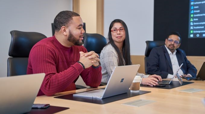 Coworkers talking at a conference table with their laptops open