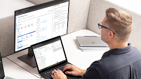 Person typing on laptop while looking at larger monitor.