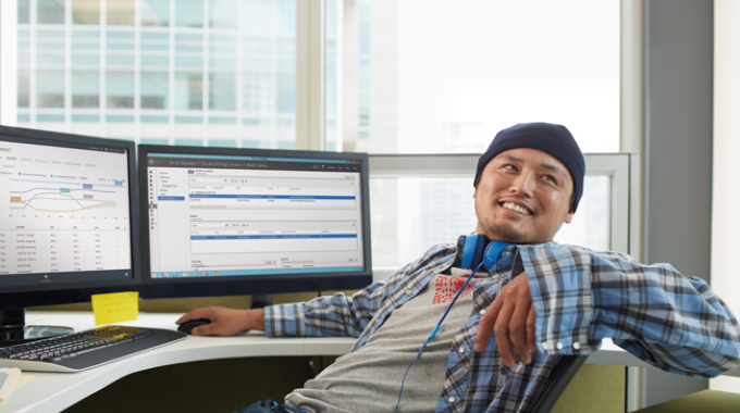 Man sitting at desk at two monitors turning and smiling