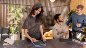 Person on a tablet while colleagues chat nearby.