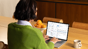 A person sitting at a dining room table types on a laptop.